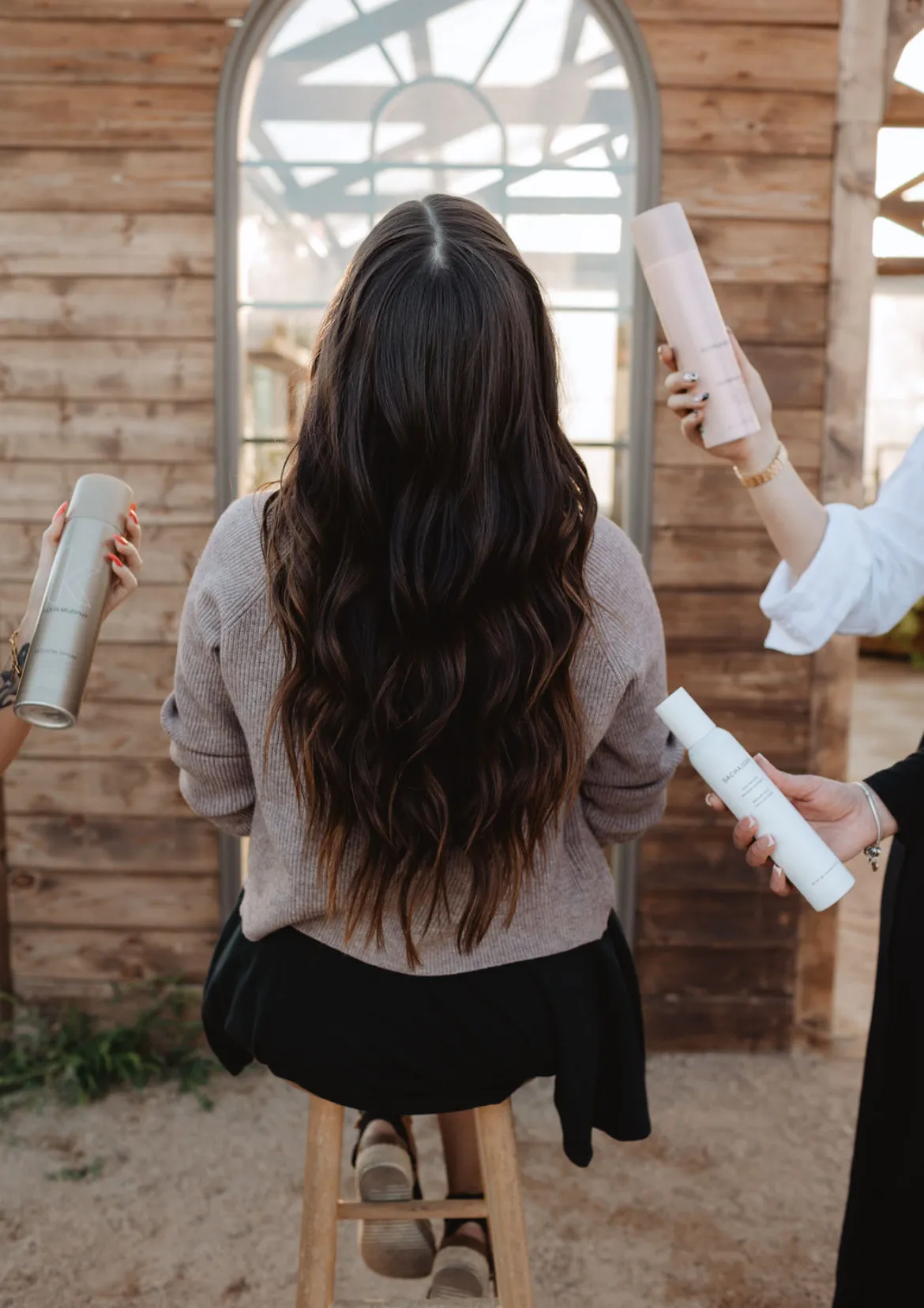 Stylists holding products around a client with long brunette waves