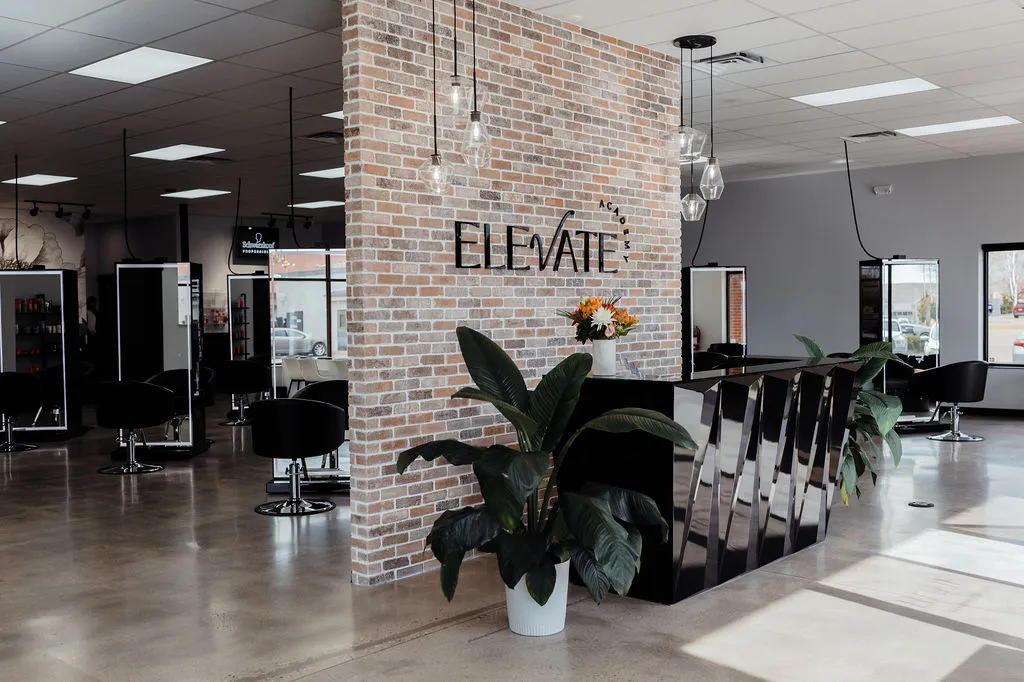The Elevate Academy salon floor in Windsor, Colorado, with styling stations and the brick feature wall